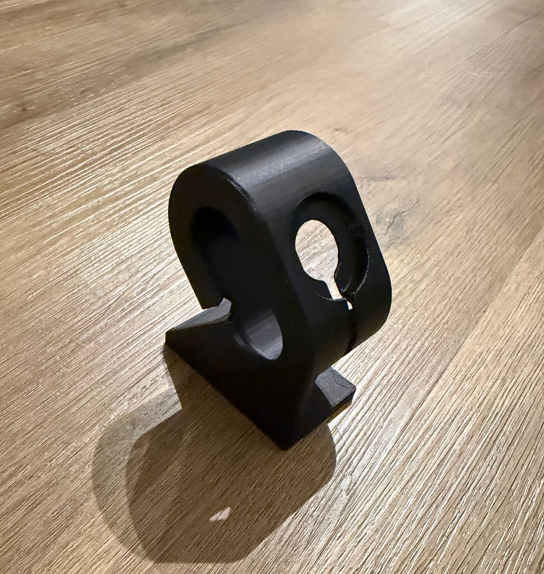 Zwarte kunststof montagebeugel met een ronde opening, die op een houten ondergrond staat.