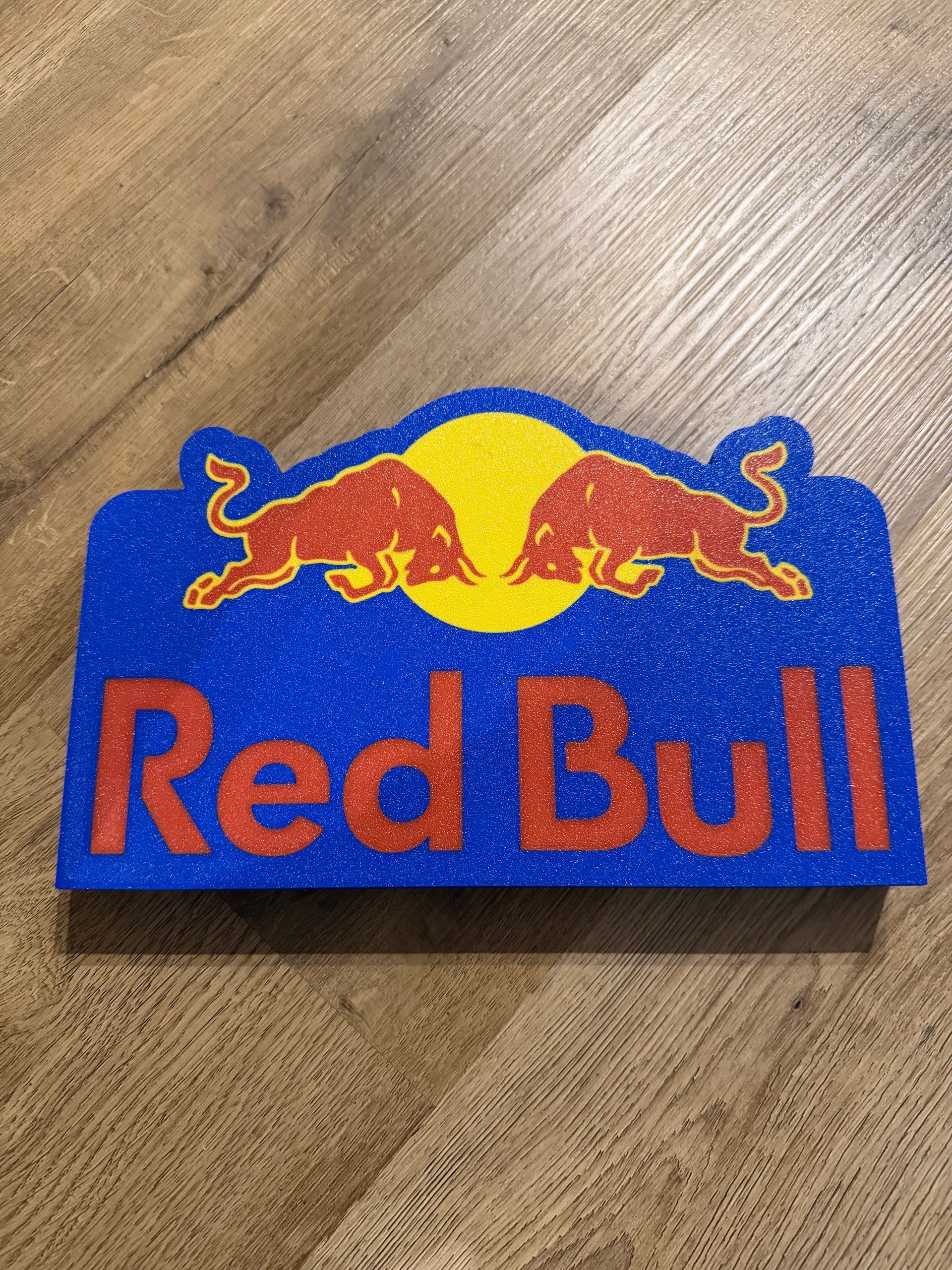 Red Bull-logopatch met blauwe en rode tekst op een houten ondergrond.