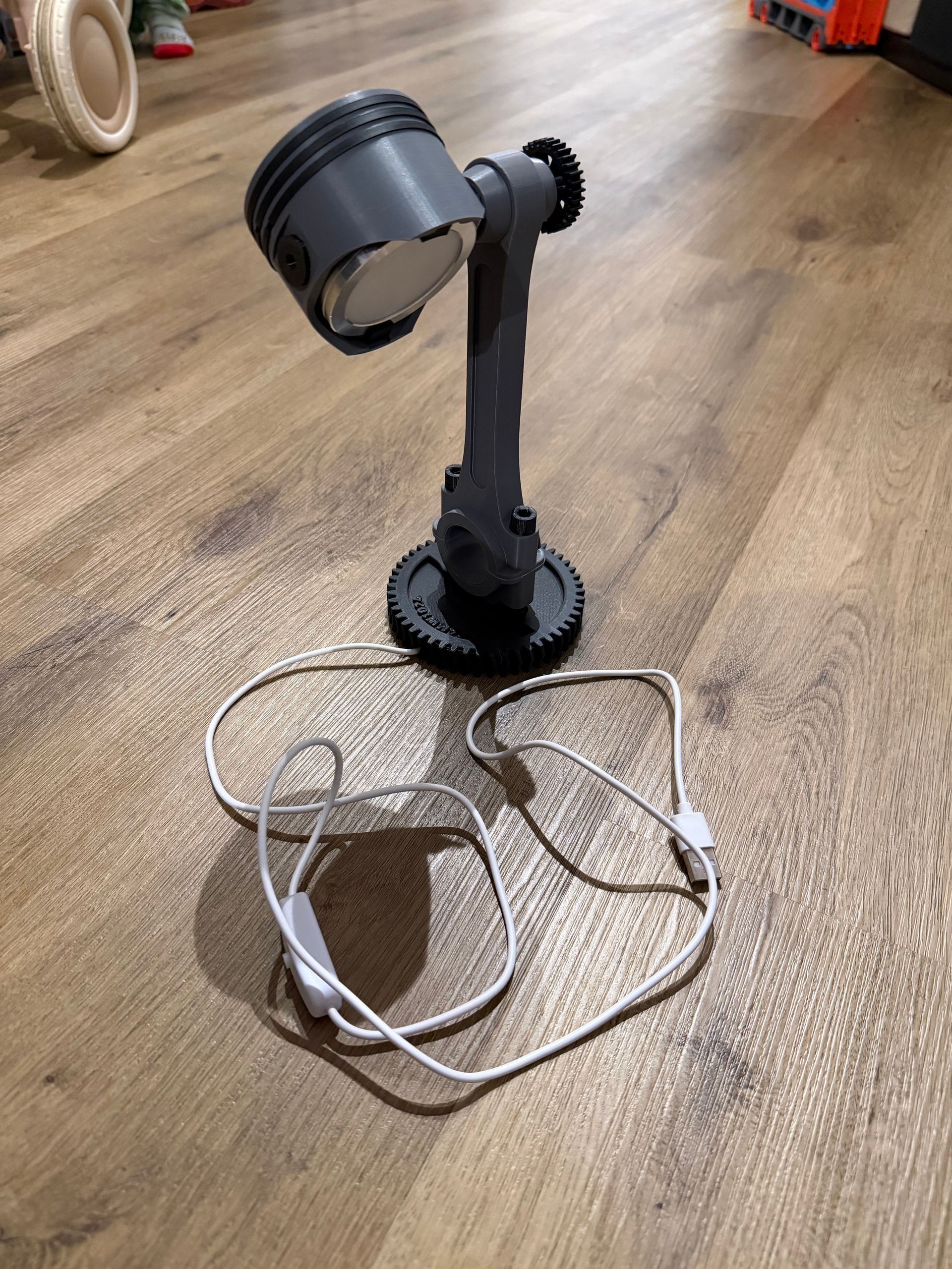 Zwarte staande lamp op een houten vloer naast een warrig wit snoer en een bruine gevlochten mand.