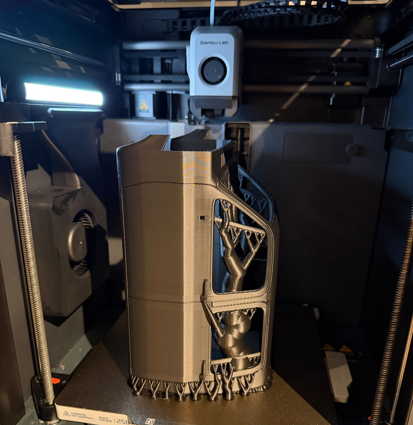 De Bambu Lab 3D-printer print een cilindrisch onderdeel van metaalzilver met ondersteunende structuren.