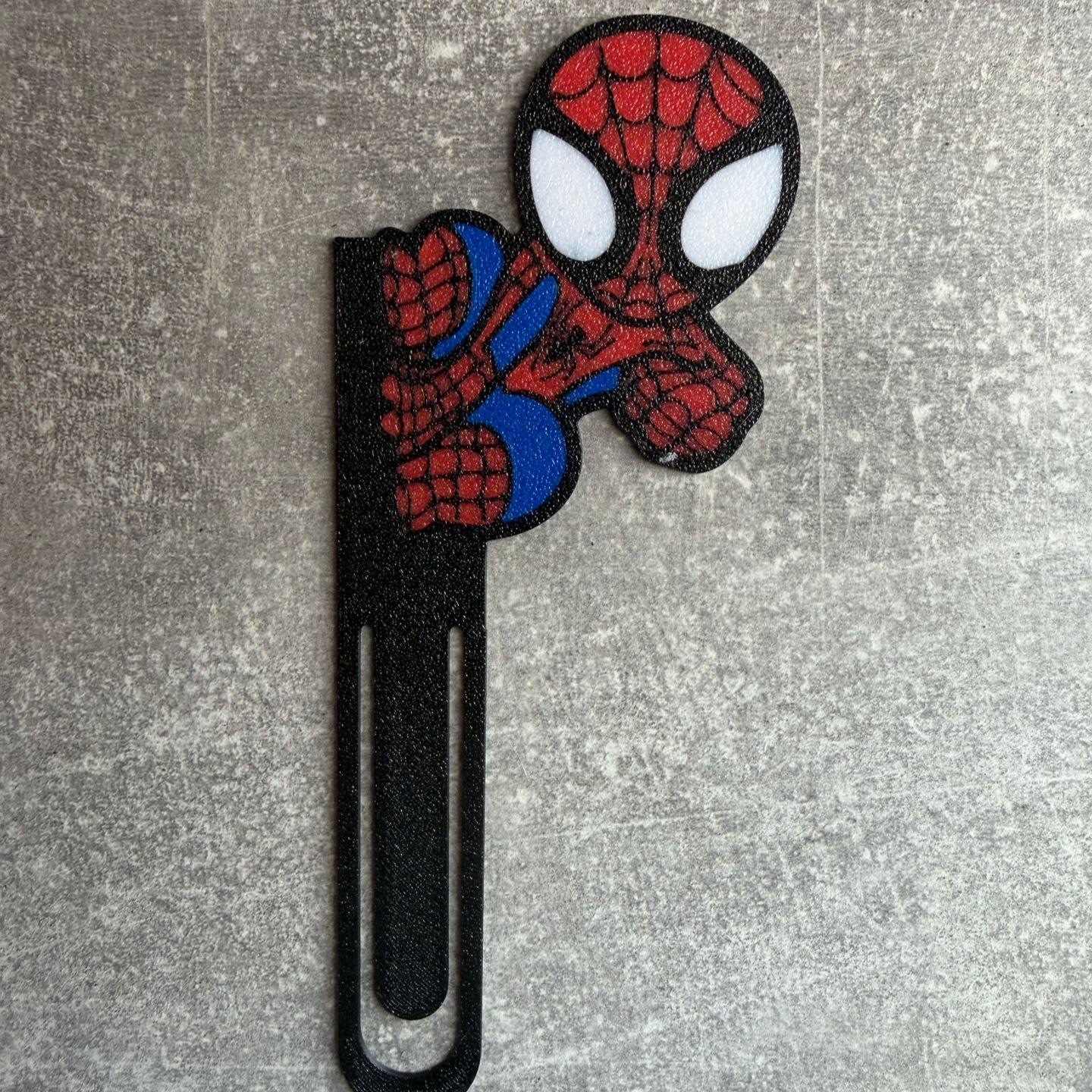 Spider-Man boekenlegger met zwarte metalen clip op een grijze achtergrond.