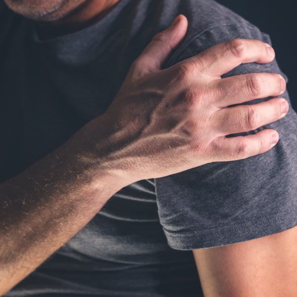 Person holding shoulder in pain, wearing a dark gray shirt.