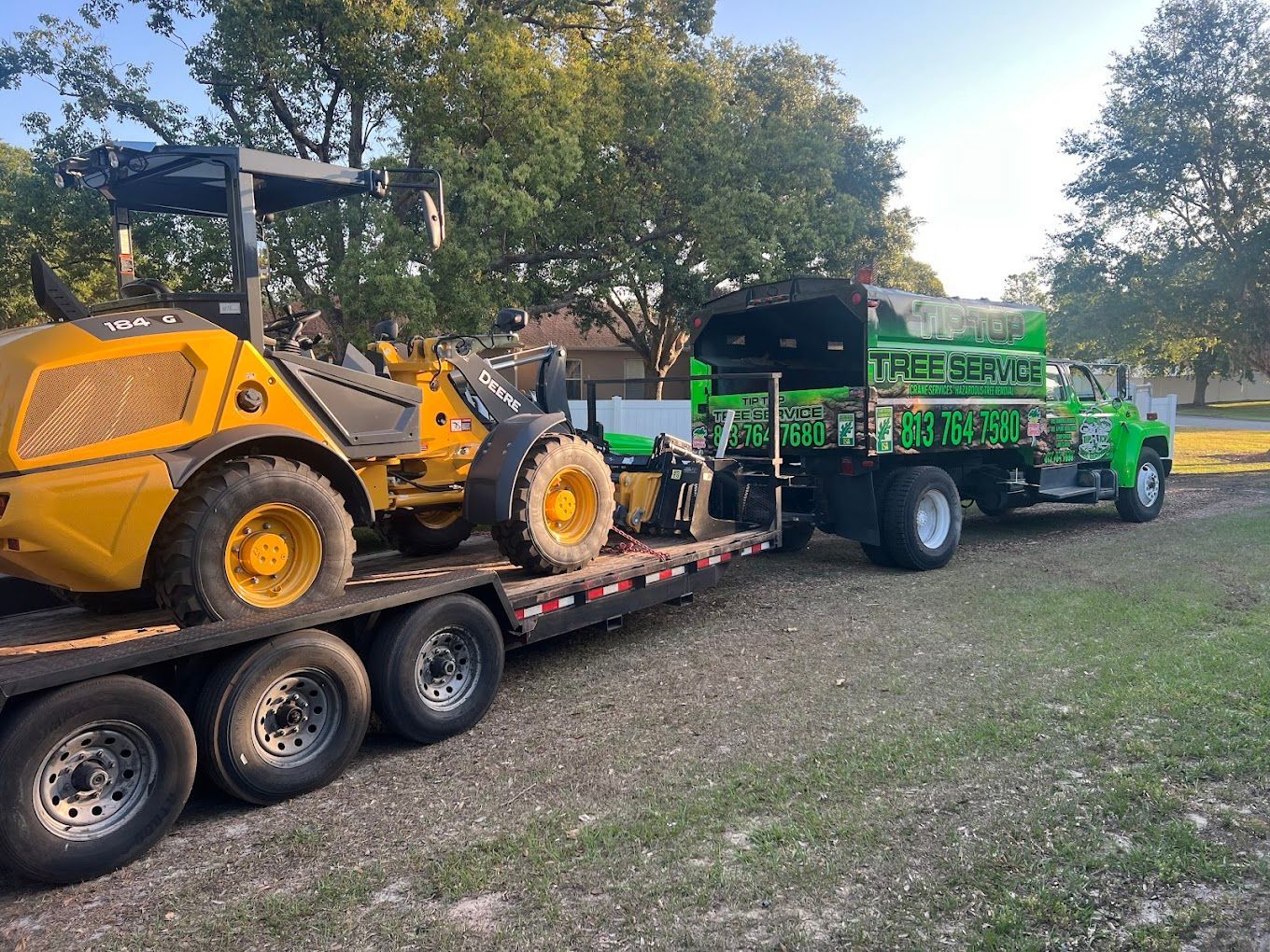 Yellow construction equipment loaded on a trailer, connected to a green truck on grass.