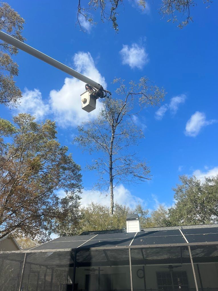 A security camera mounted on a pole, overlooking a screened-in pool area, against a blue sky with clouds.