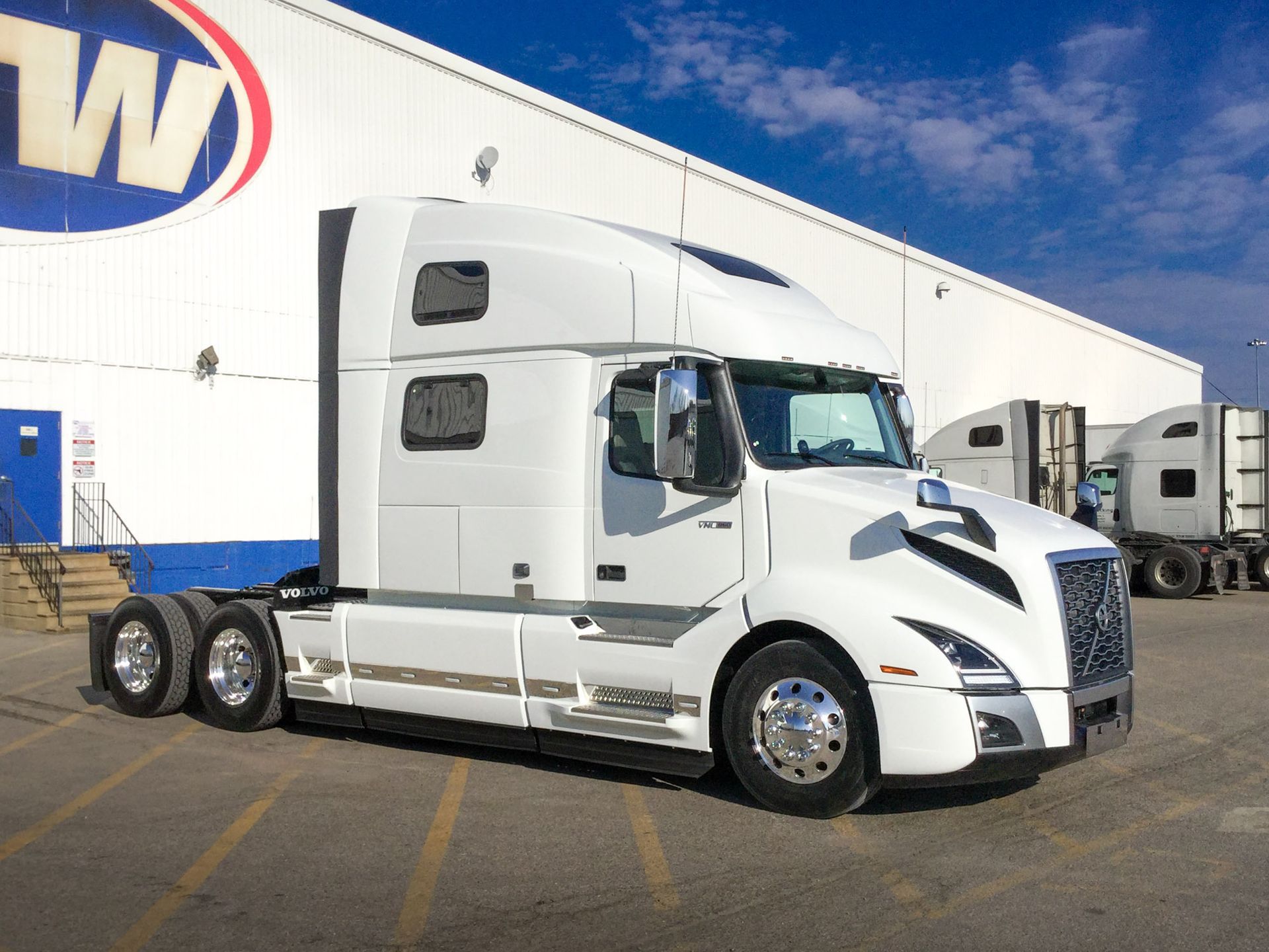 White semi-truck parked outside a warehouse under a blue sky