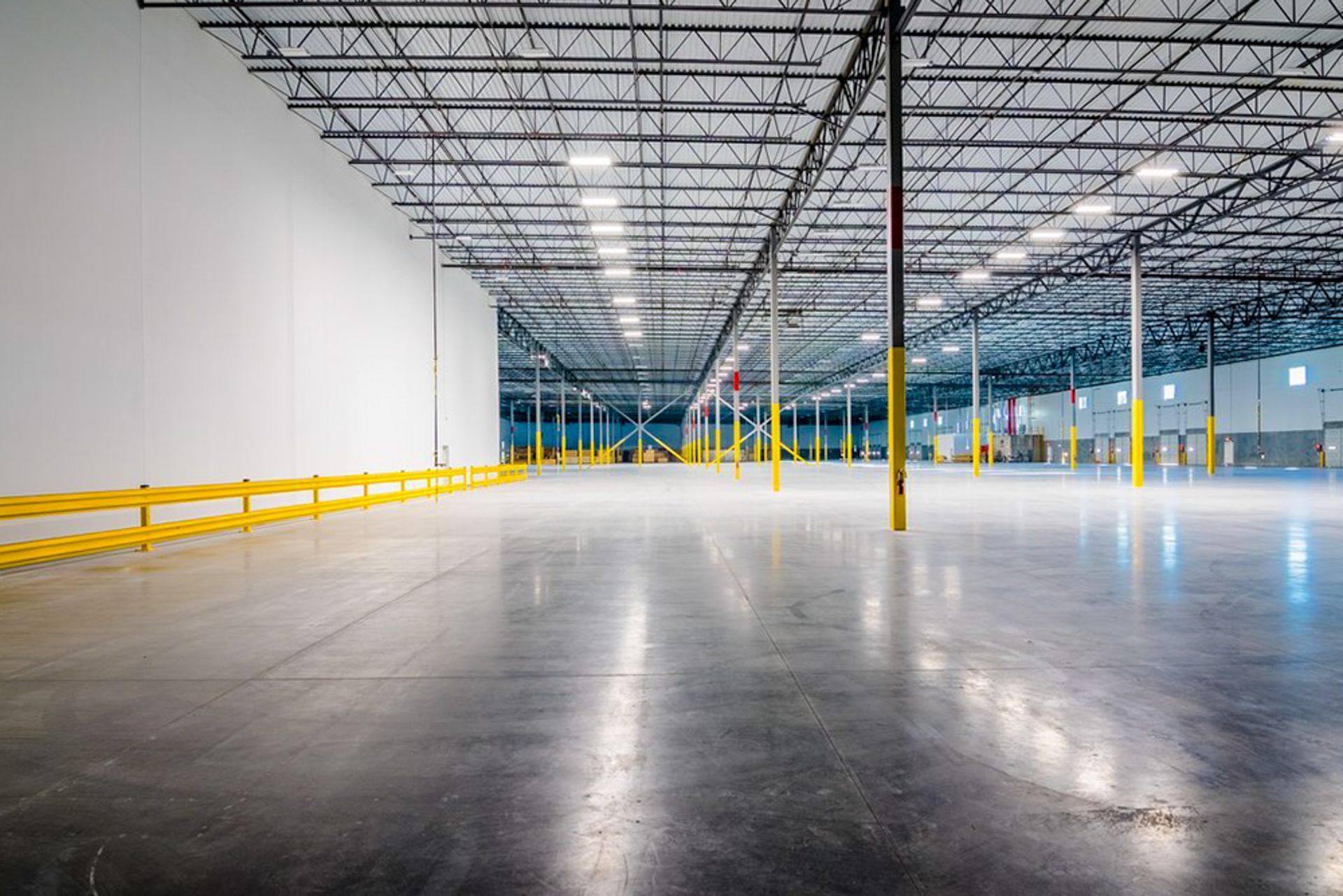 Empty warehouse interior with polished concrete floor, yellow safety rails, and exposed ceiling beams