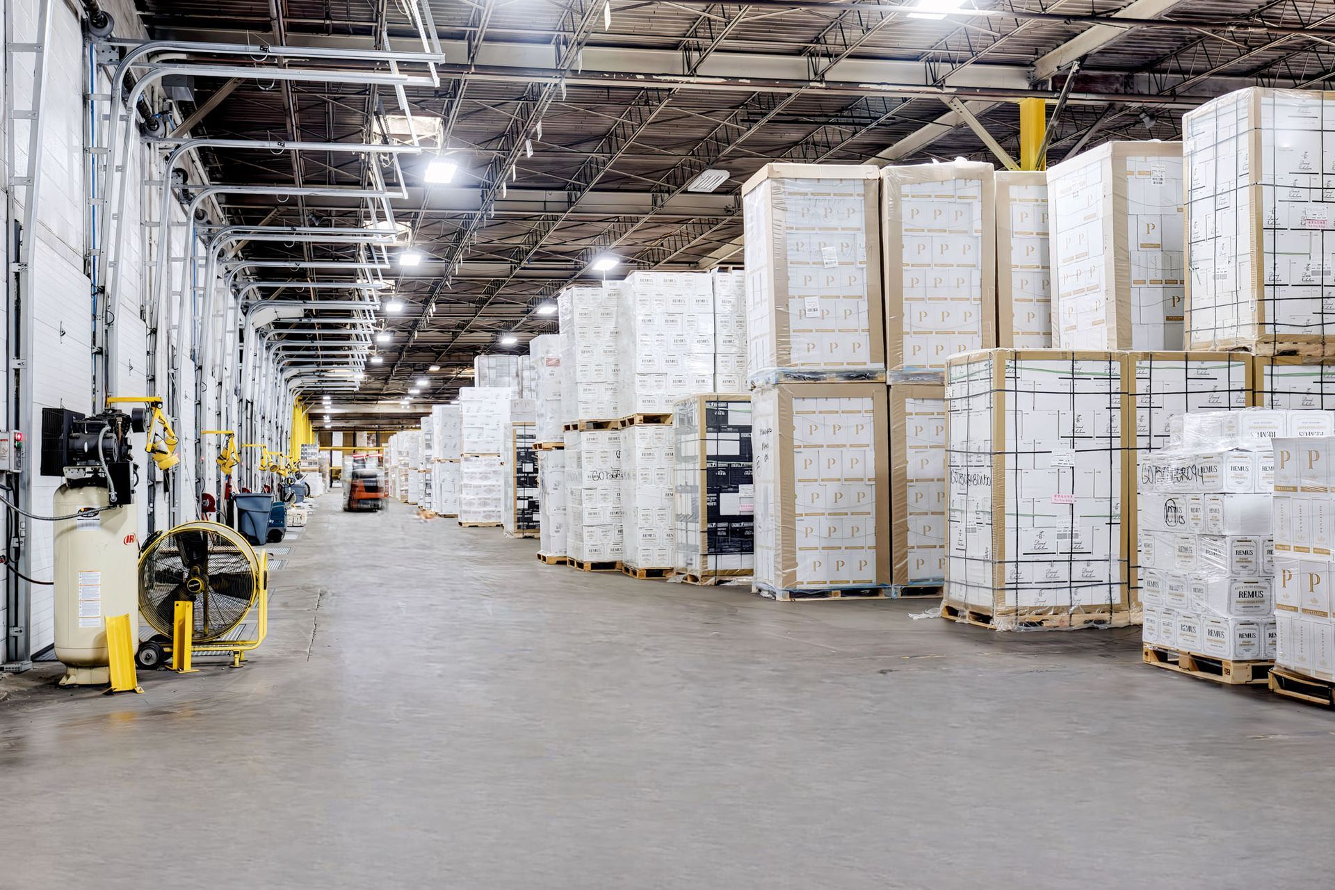 Large warehouse aisle with stacked white pallets and boxes under bright industrial lighting