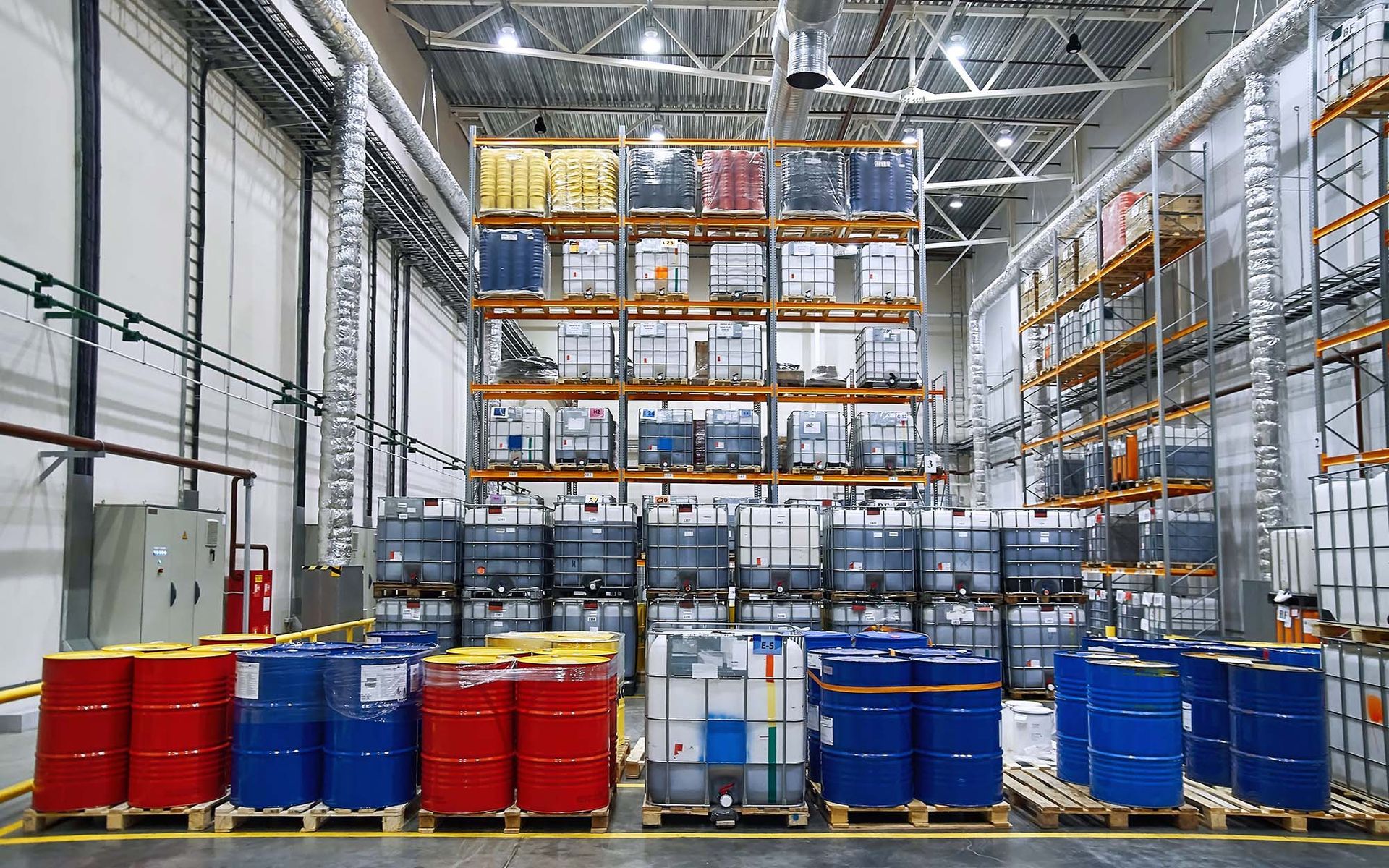 FW warehouse hazmat aisle with stacked pallets, red and blue barrels, and tall shelving