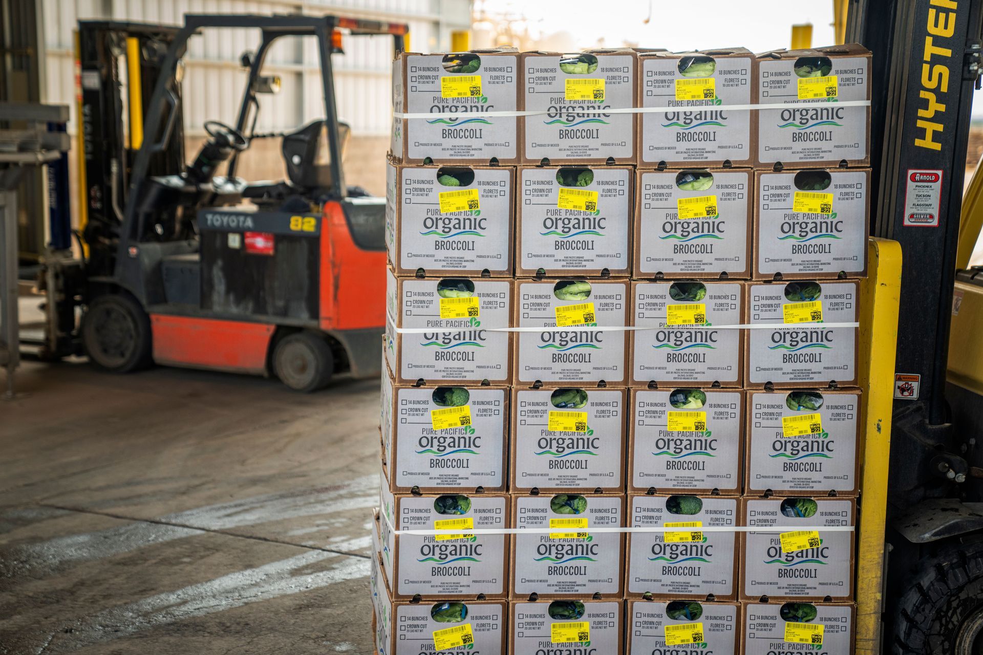 Forklift carrying stacked boxes in a warehouse with a Hyster lift on the side