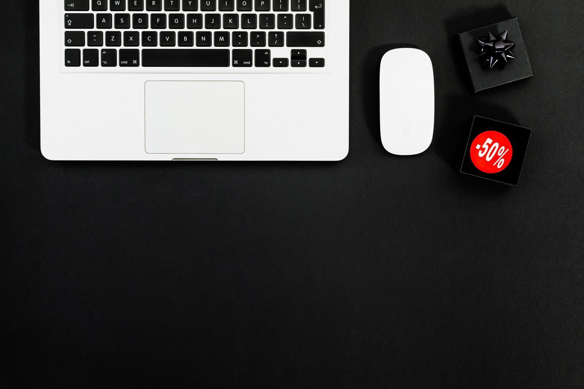 Laptop with mouse, small black box, and red smartwatch on a dark desk background