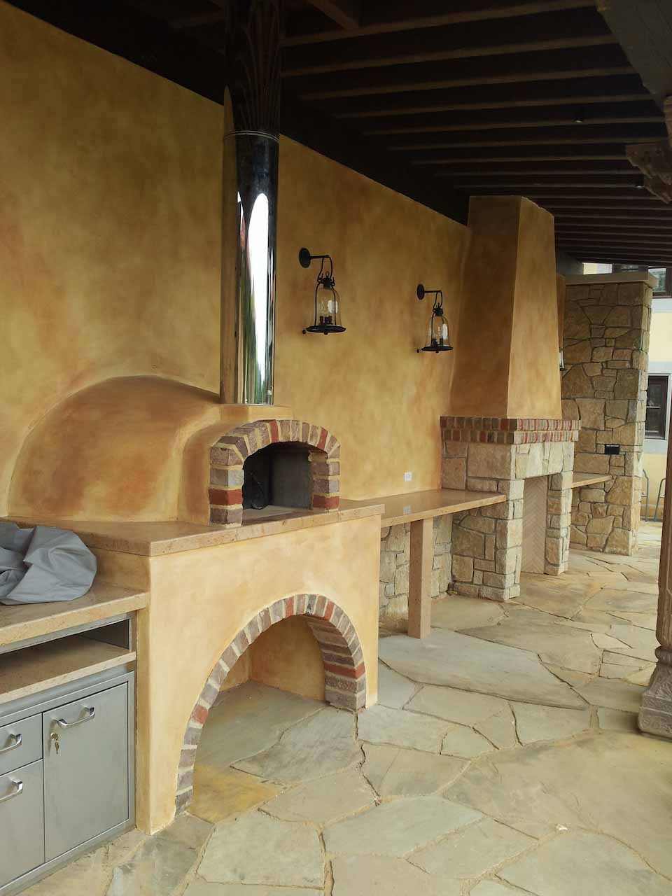 photo of an outdoor porch with fireplace and pizza oven, all decorated with venezia stucco orange lime paint and stones