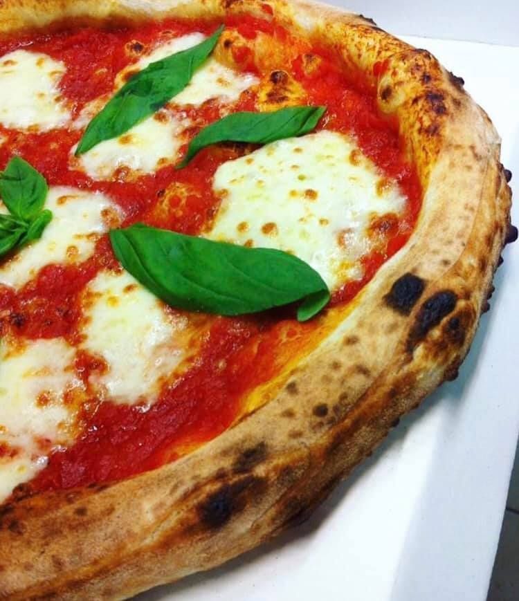 Pizza Margherita con foglie di basilico, formaggio fuso e salsa di pomodoro su un piatto bianco.