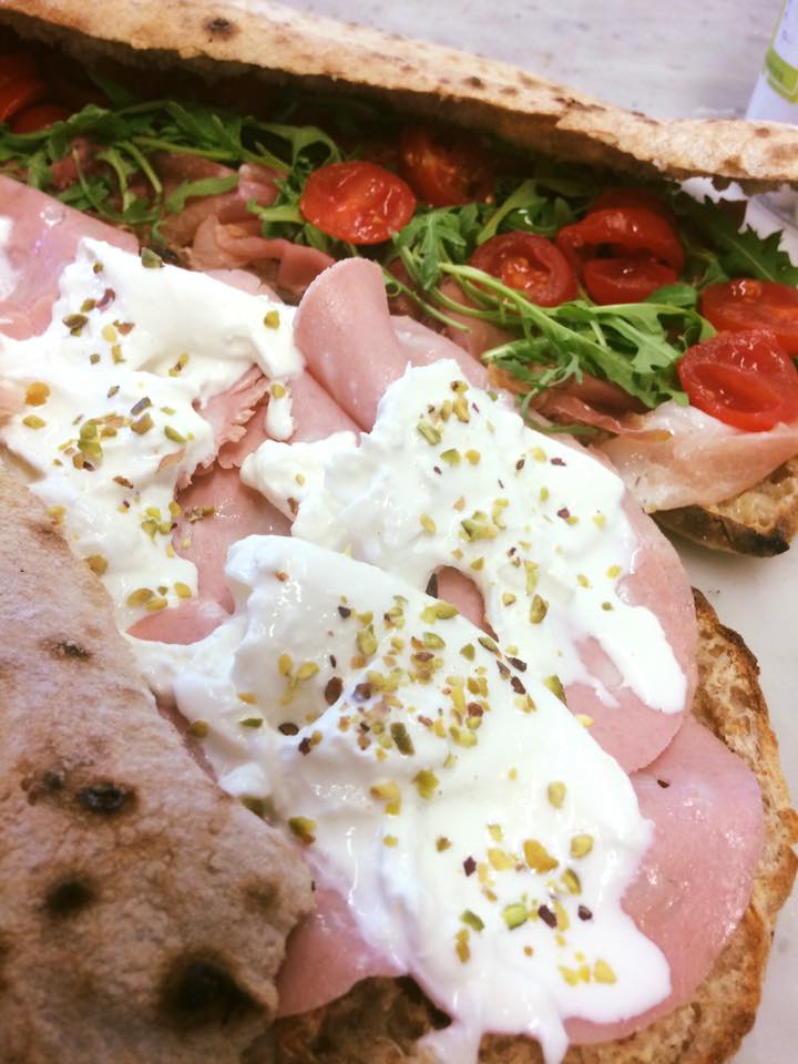 Primo piano di un panino con prosciutto e pomodori su un piatto.