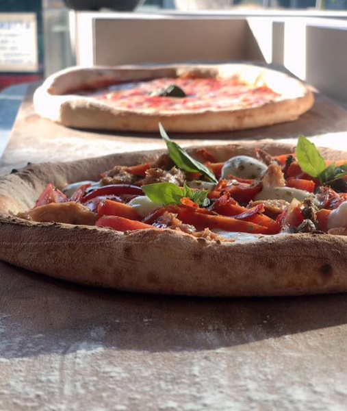 Due pizze su un tavolo, una con pomodori e basilico in primo piano, l'altra semplice sullo sfondo.