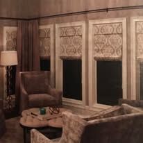 Cozy living room with plaid chairs, round coffee table, floor lamp, and lace-covered windows in warm lighting