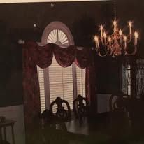Dim dining room with chandelier, arched window, and dark wood chairs by a curtained window.