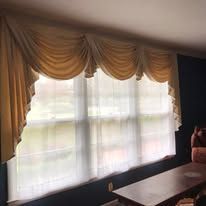 Gold draped curtains over a large bright window above a dark table in a room
