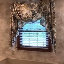 Floral valance and side drapes framing a small window with white blinds and a wooden frame.