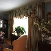 Elegant living room with bay window, floral drapes, and potted plants, lit by bright daylight