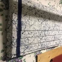Floral window shade with lace curtain and blue trim against patterned wallpaper