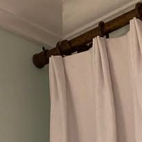 White curtains hung on a dark wood curtain rod near a ceiling corner.