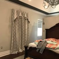 Bedroom with dark wood bed, patterned curtains, beige walls, and a chandelier overhead.