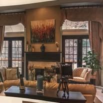 Cozy living room with a fireplace, large windows, curtains, sofa, and a tripod in the center.