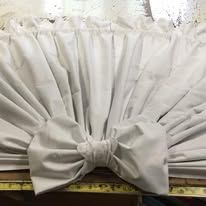 White curtains tied in a large bow at the bottom, covering a window or opening