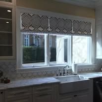 Kitchen sink under a window with patterned valance and gray cabinets