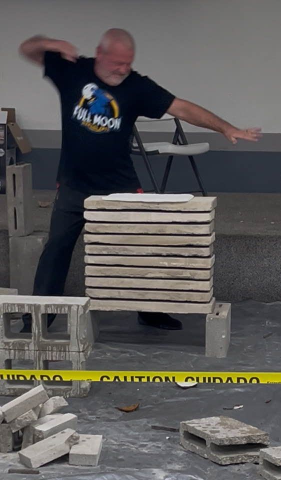 Man breaking stacked bricks with his hand. Yellow caution tape in the foreground. Concrete setting.