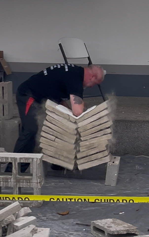 Man breaking stacked cinder blocks with his elbow. Dust and debris fill the air.