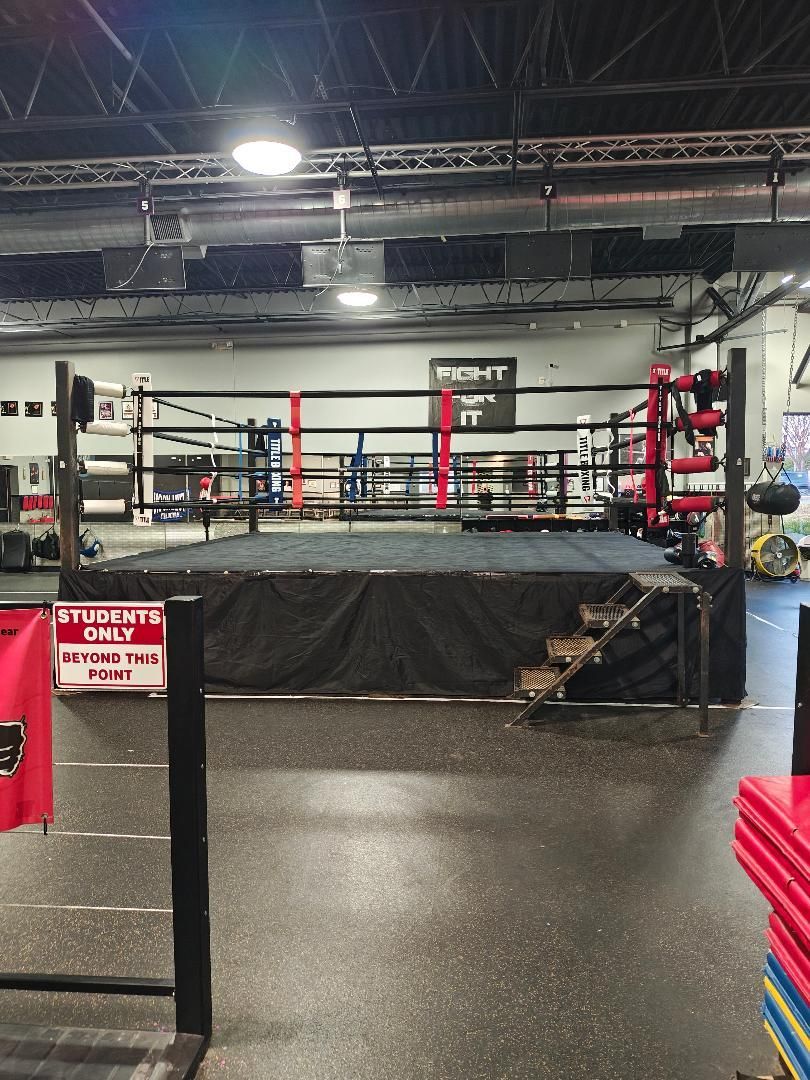 Empty boxing ring in a gym with red corner posts and black padded apron