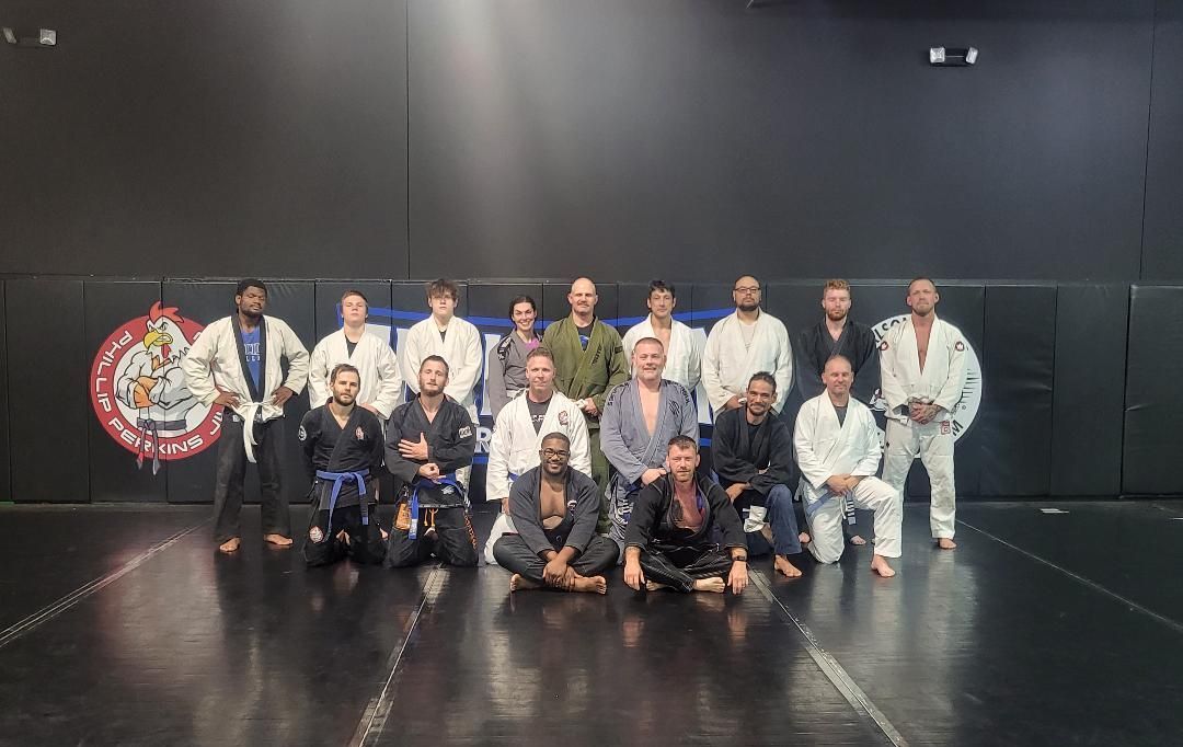 Group of people in martial arts attire posing on a mat in a gym.