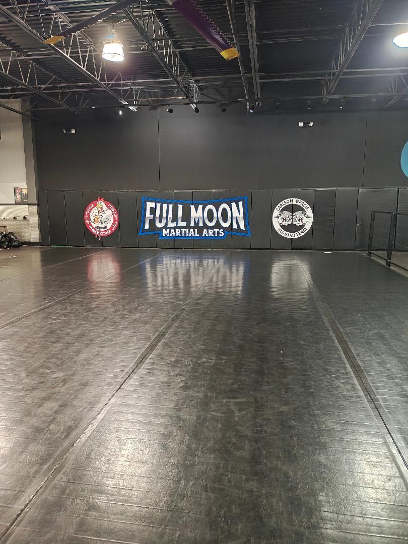 Empty black gym mat with a “Full Moon” banner on the back wall in a dim training studio