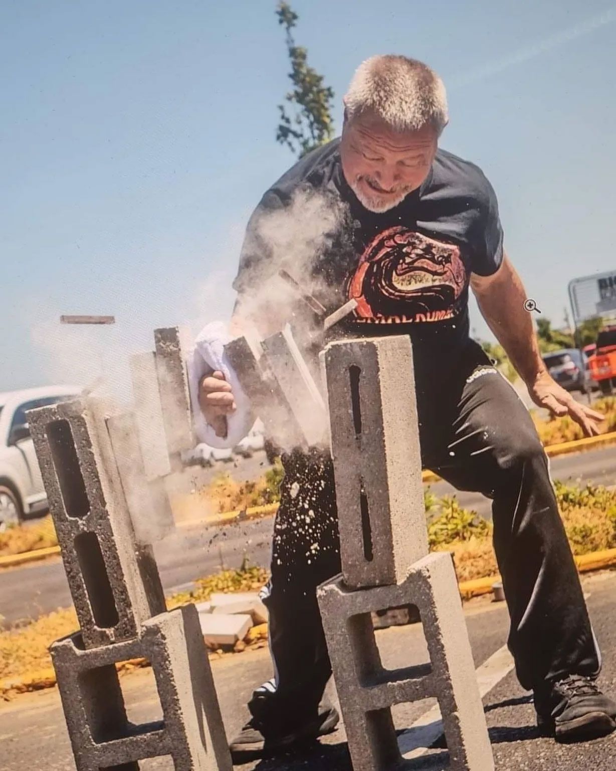 Man breaking concrete blocks with his hand, outdoors. Dust and debris flying.