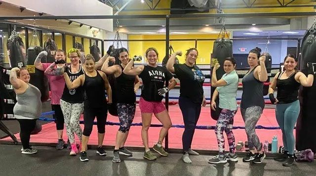 Group of women flexing muscles at a gym, posing in front of punching bags.