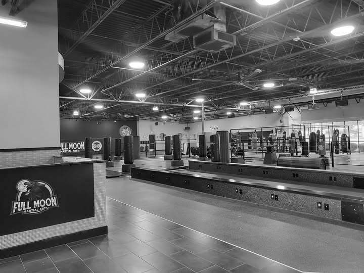 Spacious empty gym with weight machines, mirrored walls, and a dark tiled floor under bright ceiling lights