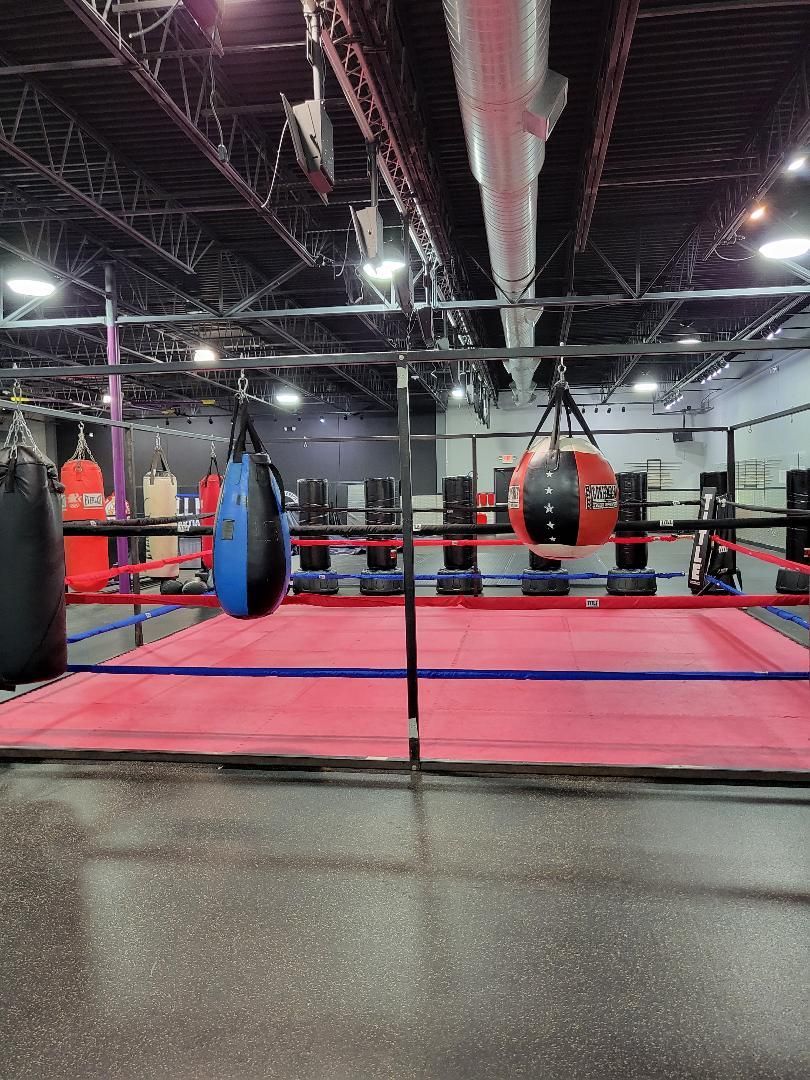 Boxing gym interior with a boxing ring, punching bags, and industrial ceiling.