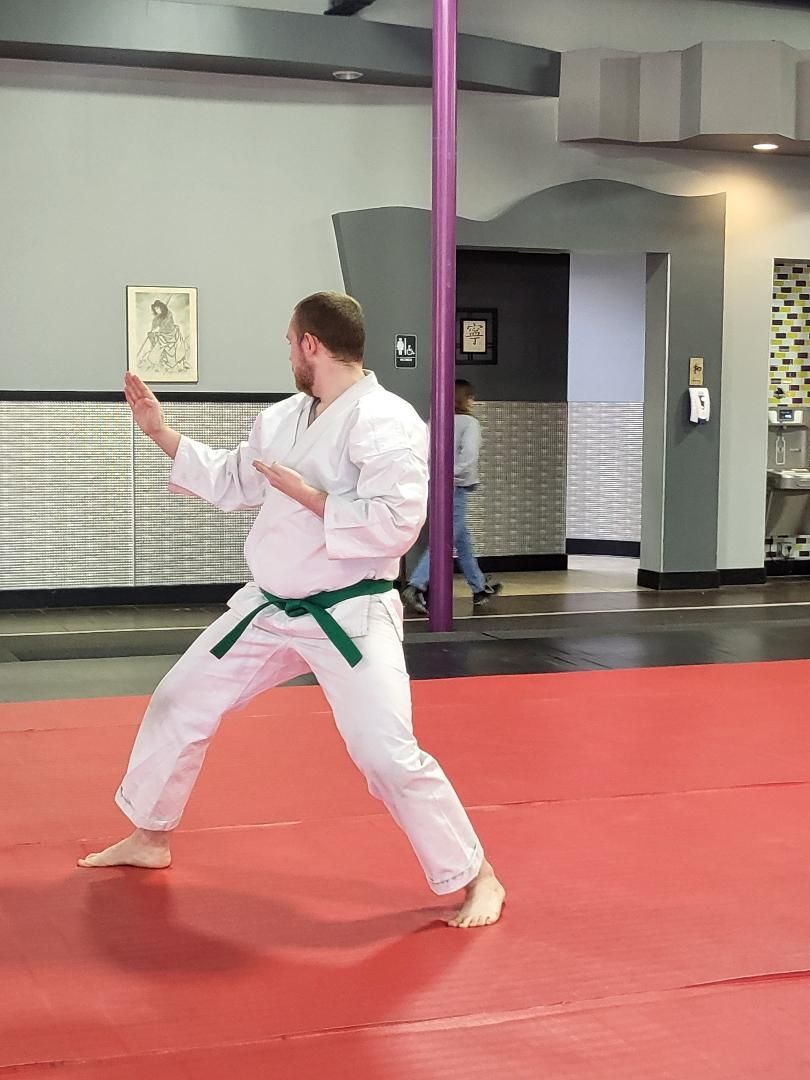 Man in white karate uniform with green belt in a fighting stance on a red mat.