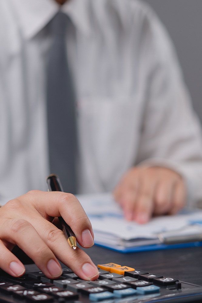 Person in a white shirt and tie using a calculator, pointing a pen at the numbers.