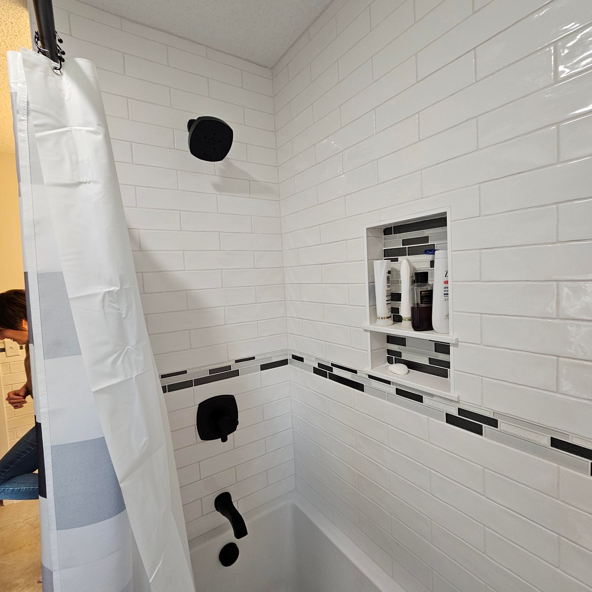 A man is standing in a bathroom next to a shower curtain.