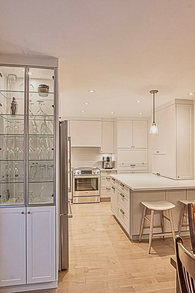 Cuisine moderne avec armoires blanches, appareils électroménagers en acier inoxydable et vitrine.