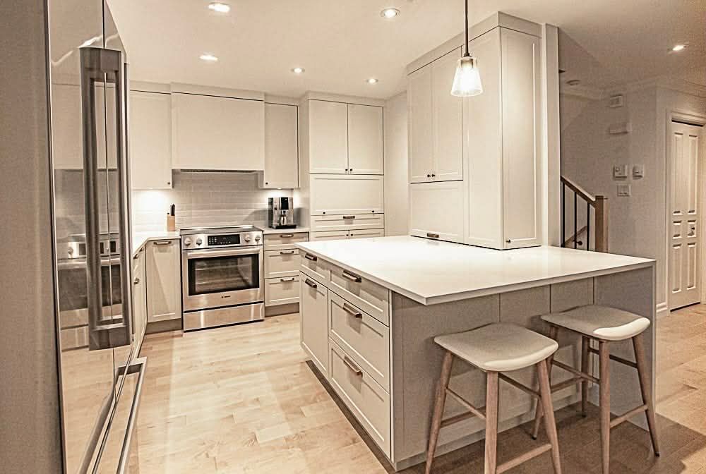Cuisine blanche moderne avec îlot central, appareils électroménagers en acier inoxydable et parquet.