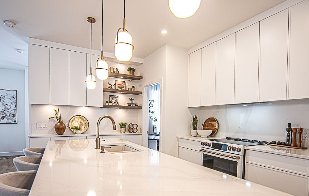 Cuisine blanche moderne avec îlot central, placards, étagères, suspensions lumineuses et appareils électroménagers en acier inoxydable.