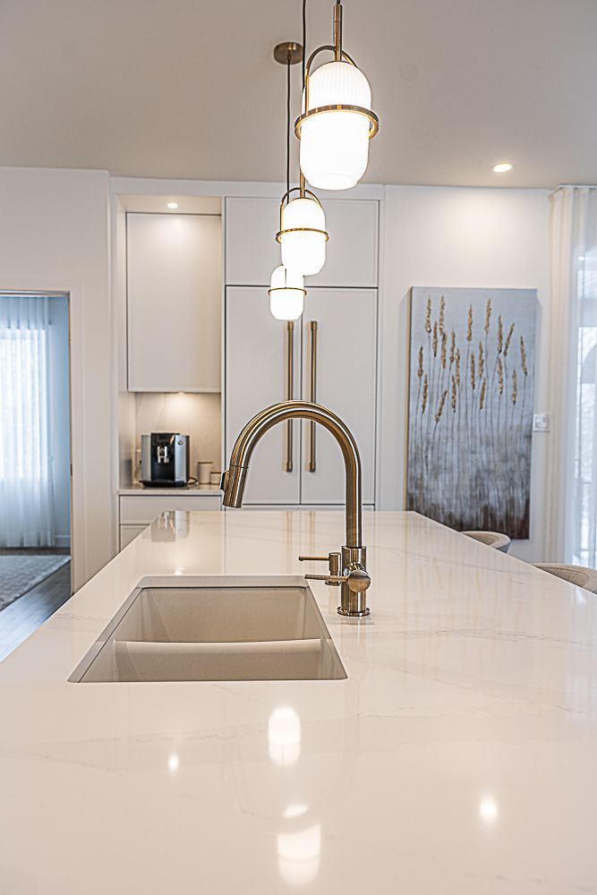 Cuisine moderne avec comptoirs blancs, évier, robinet doré et luminaires suspendus en forme de globe.