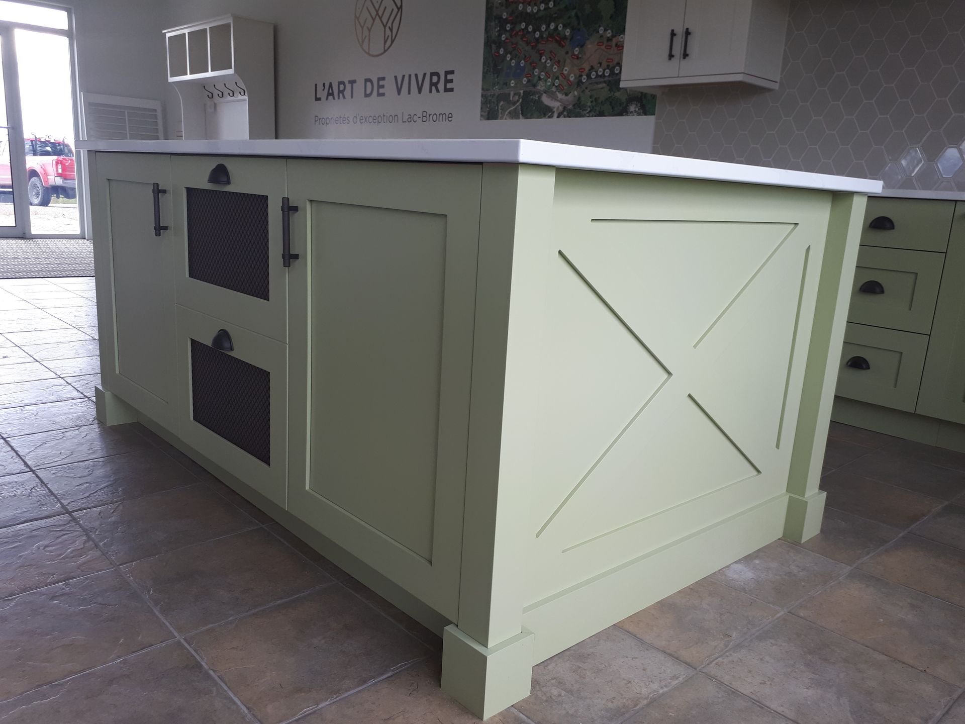 Îlot de cuisine vert avec plan de travail blanc. Comprend des portes d'armoires, des tiroirs et un panneau décoratif en forme de X.