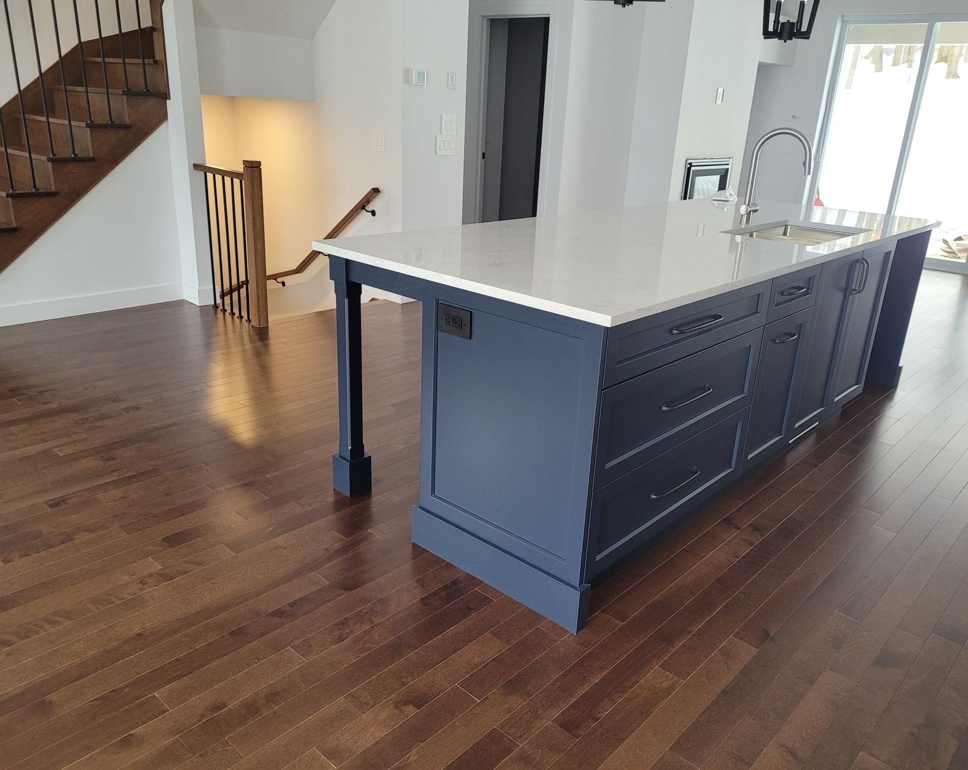 Îlot de cuisine bleu marine avec comptoir blanc, parquet marron, escalier visible en arrière-plan.