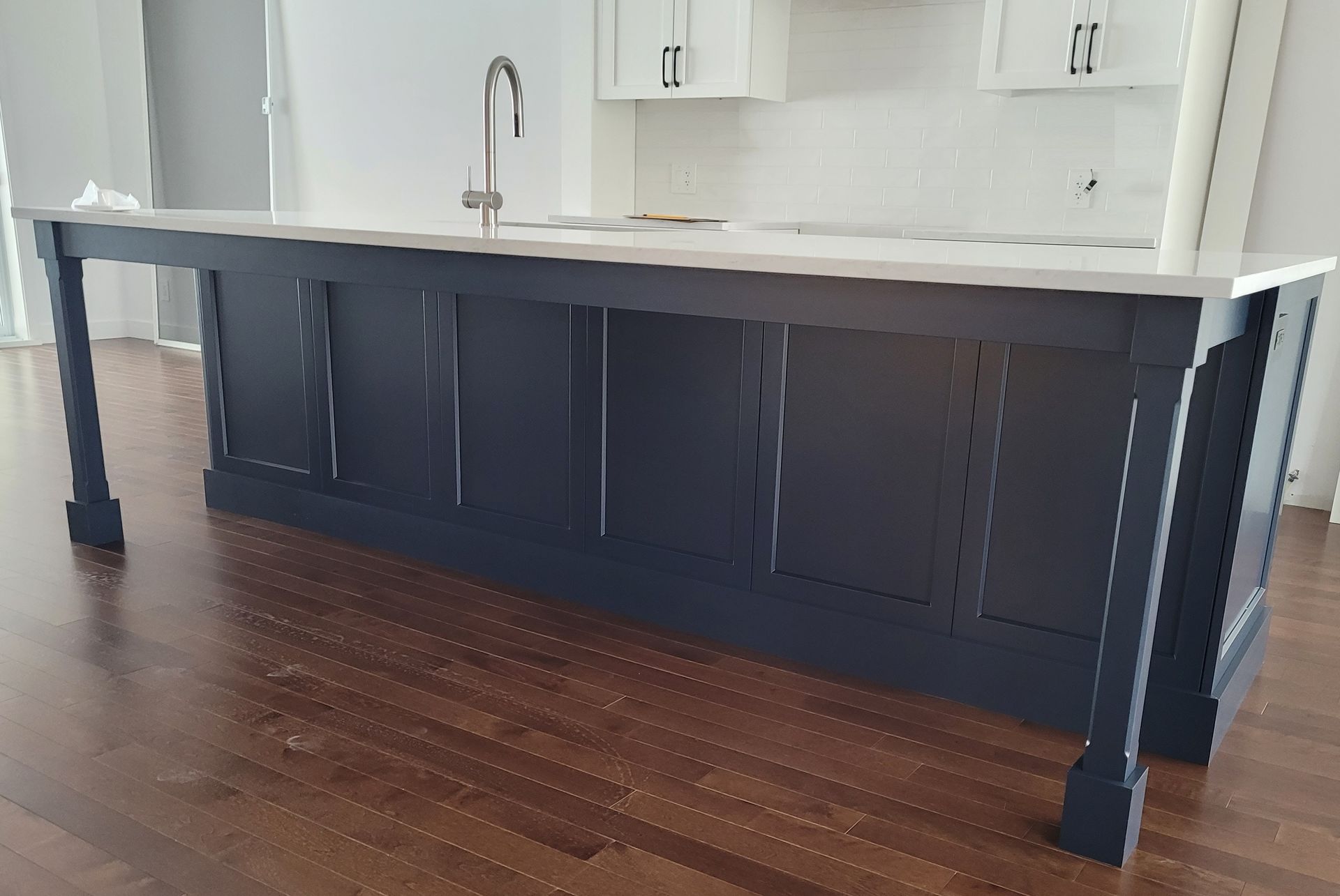 Îlot de cuisine bleu marine avec plan de travail et évier blancs, installé sur un parquet.