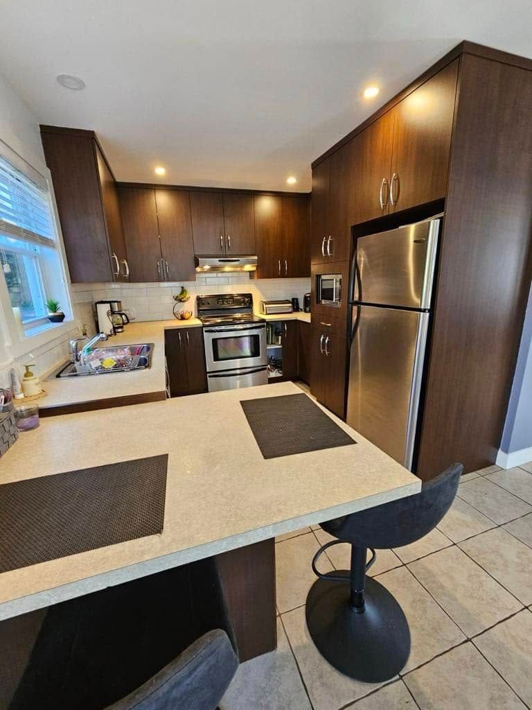 Cuisine moderne avec placards en bois foncé, appareils électroménagers en acier inoxydable et un bar à petit-déjeuner avec deux sets de table.
