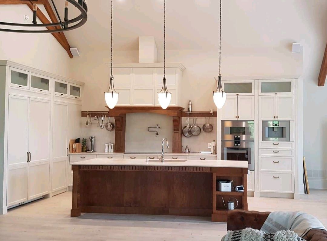 Cuisine blanche spacieuse avec îlot en bois foncé, luminaires suspendus et appareils électroménagers en acier inoxydable.